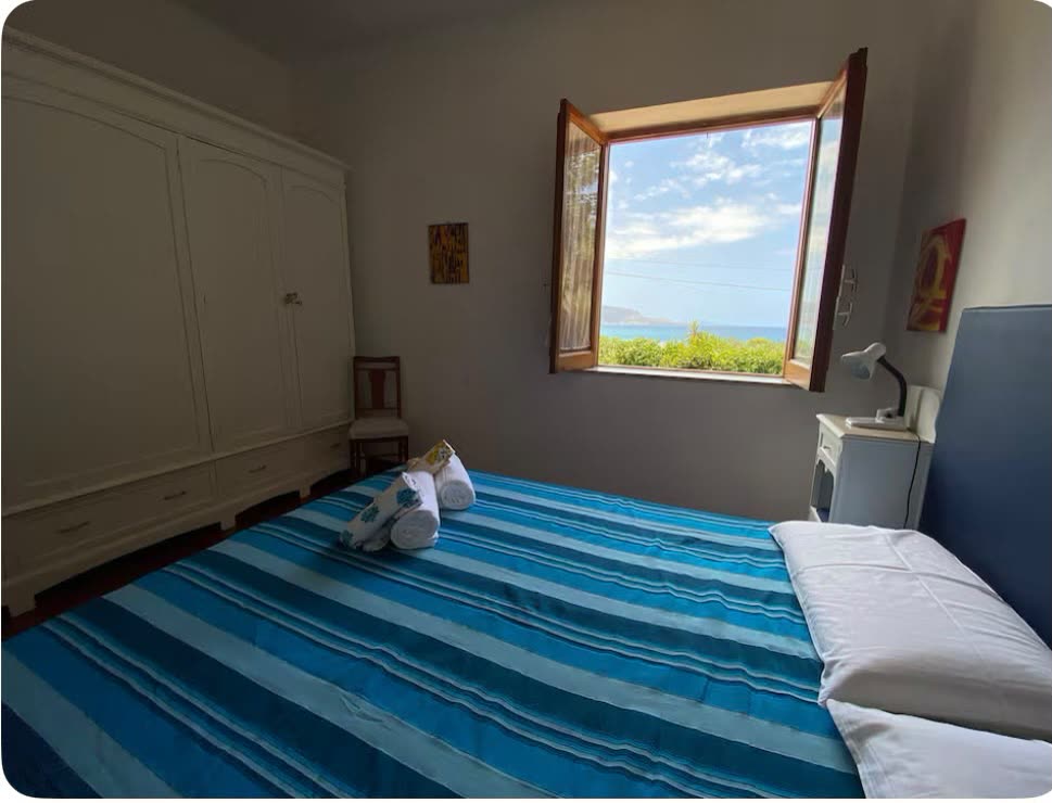 Zimmer mit blau gestreifter Tagesdecke und Fenster zum Meer